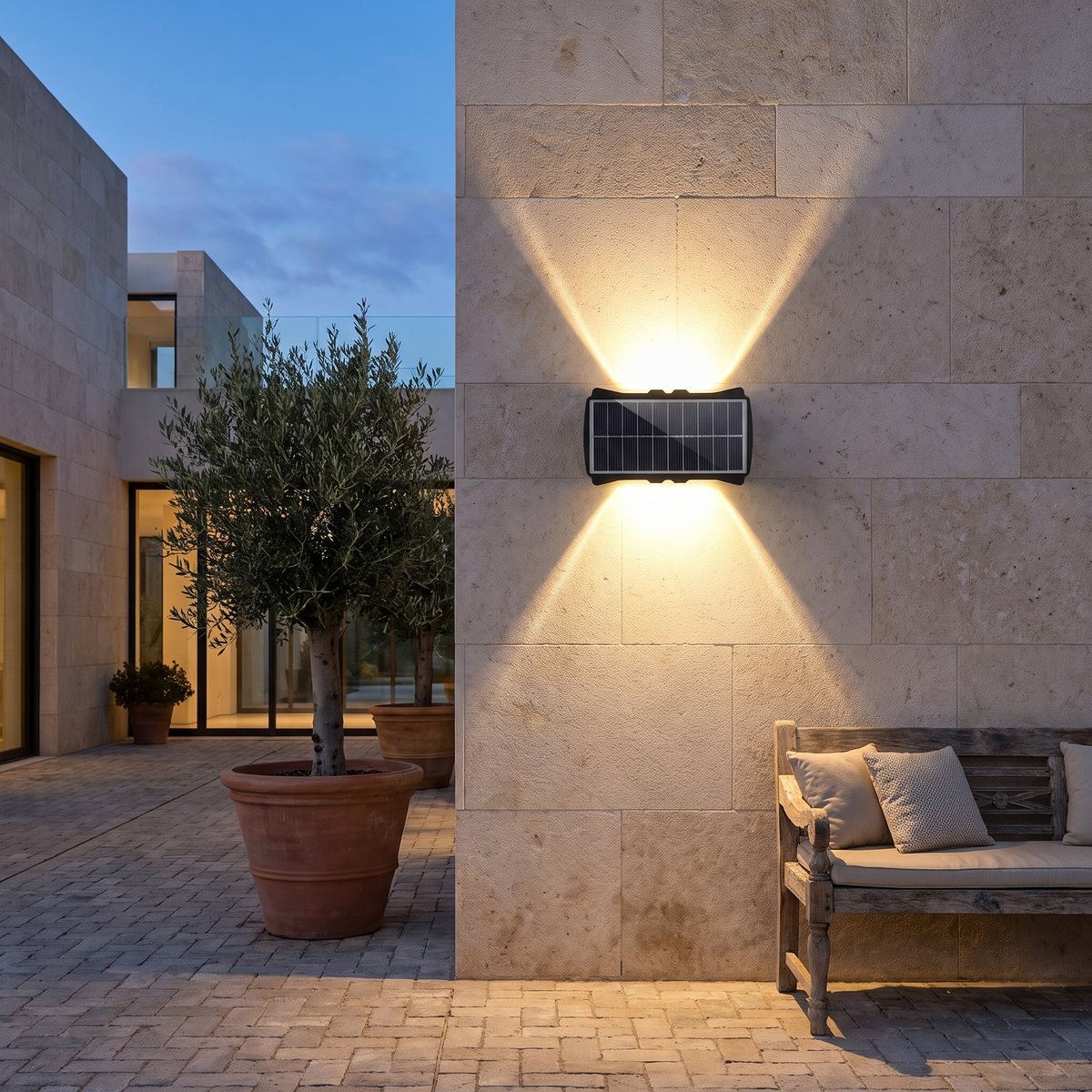 Solar up and down wall light glowing on a stone courtyard wall at dusk