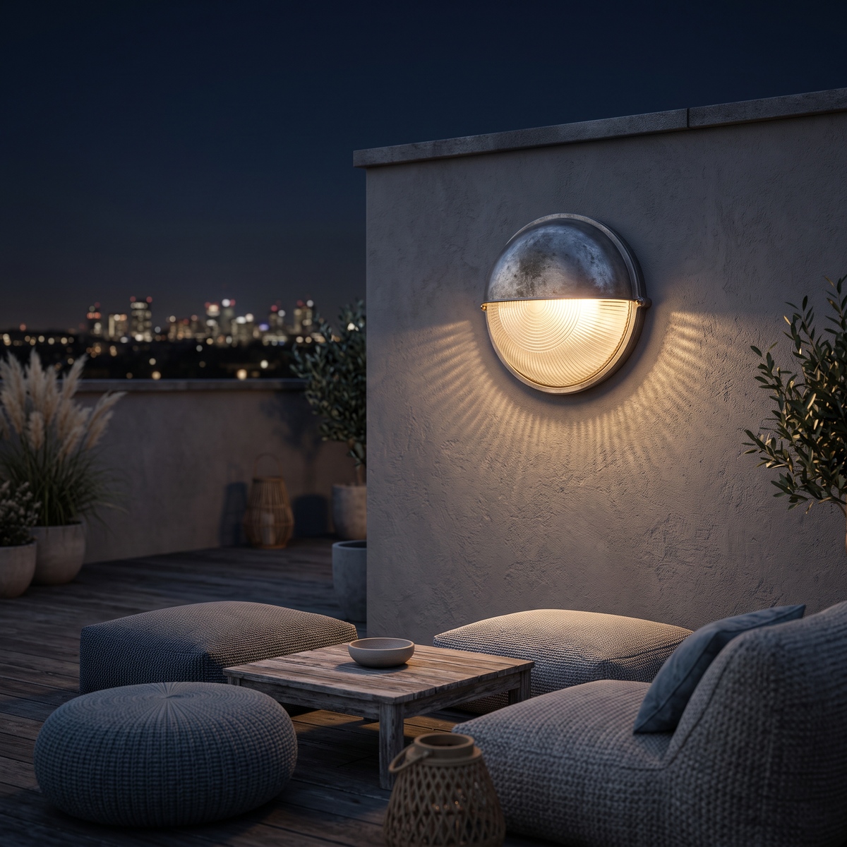 The marine bulkhead wall light on a rooftop terrace wall at night above outdoor floor cushions and a low table, glowing warm