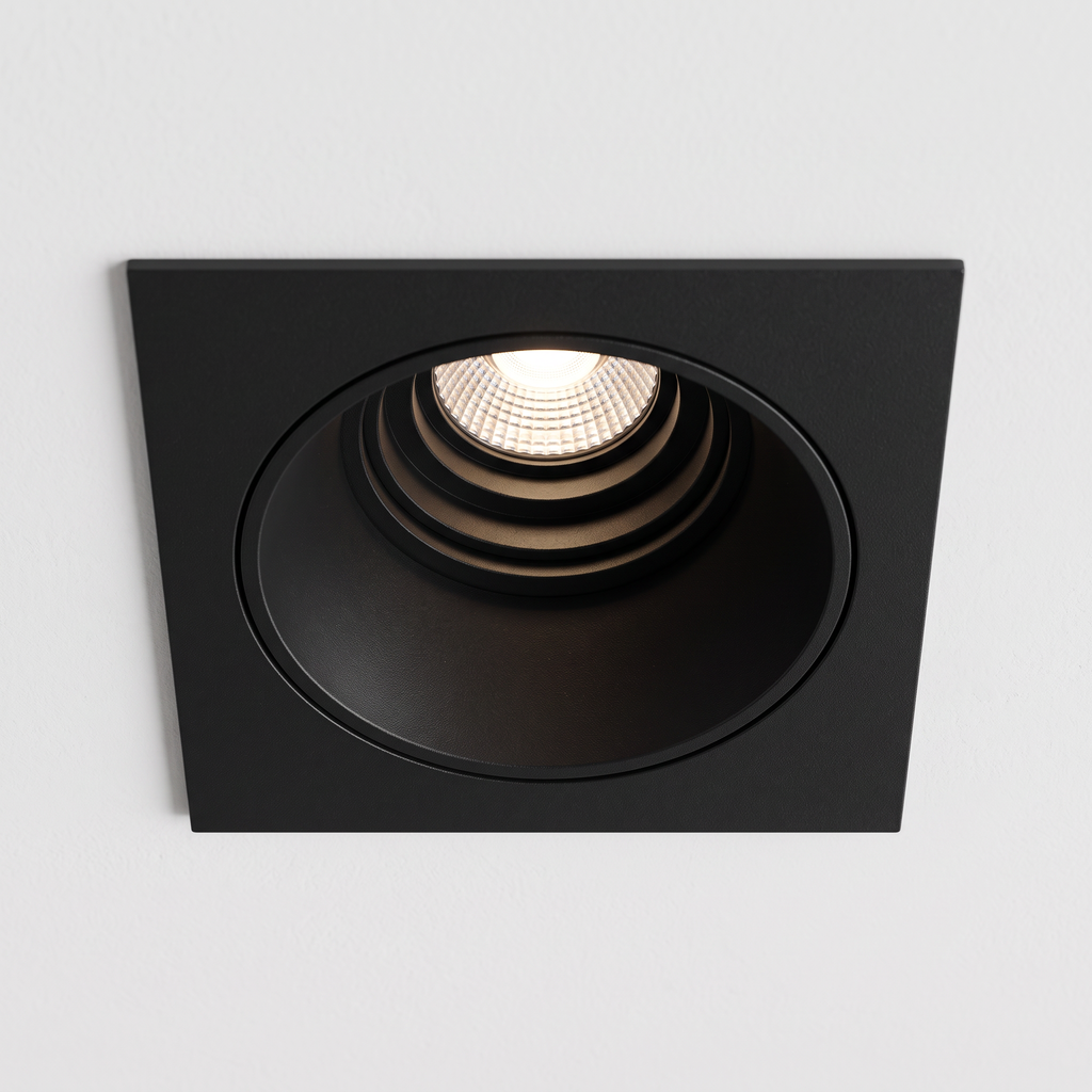 Looking up at one deep anti-glare spotlight frame lit in a white ceiling, close-up showing how the light source sits deep inside