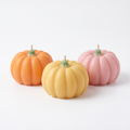 Three pumpkin shaped scented candles in orange, yellow and pink on a white background